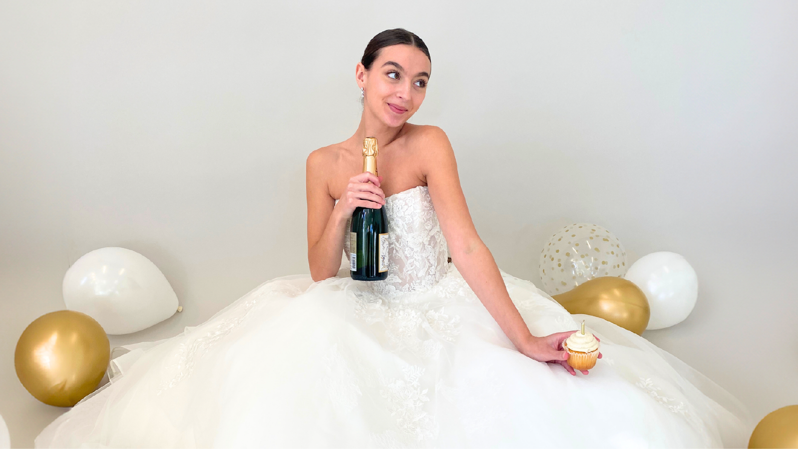 A bride celebrating with champagne, a cupcake, and white and gold balloons
