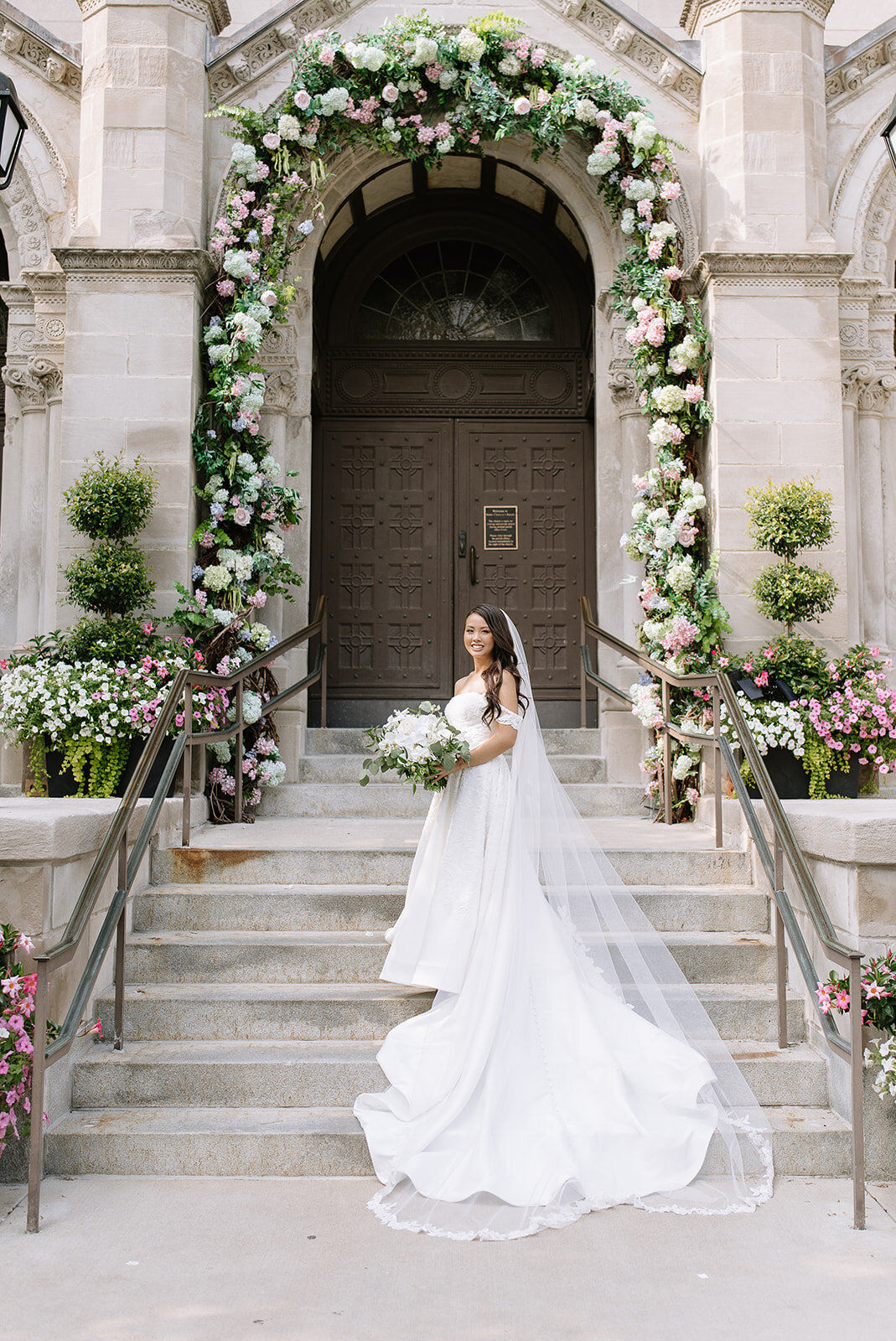 Bride in her wedding gown beneath a floral arch